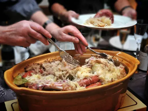 Un plat généreux de choucroute garnie, spécialité de la gastronomie alsacienne, est servi. Des mains servent ce délice, promesse d'une savoureuse nourriture d'Alsace.
