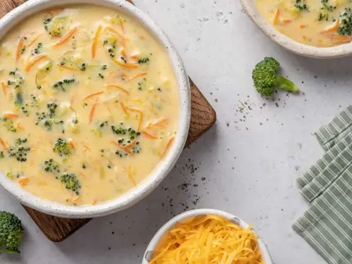 Un cremoso puré de brócoli y zanahoria, con trozos visibles de brócoli y ralladura de queso, servido en un cuenco blanco.