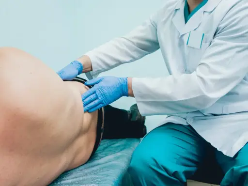 Lekarz w białym fartuchu i niebieskich rękawiczkach bada pacjenta. To badanie, które wykonuje lekarz, kto bada prostatę.