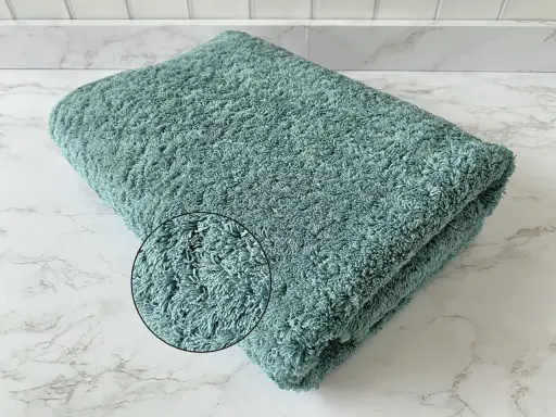 A folded teal terry cloth towel with a magnified inset showing its plush texture.