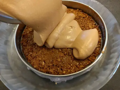 Une crème onctueuse est versée sur une base de croustillant praliné feuilletine dans un cercle à pâtisserie.