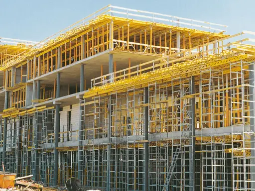 Edificio en construcción con intrincadas estructuras temporales amarillas y grises, sosteniendo los pisos de concreto.