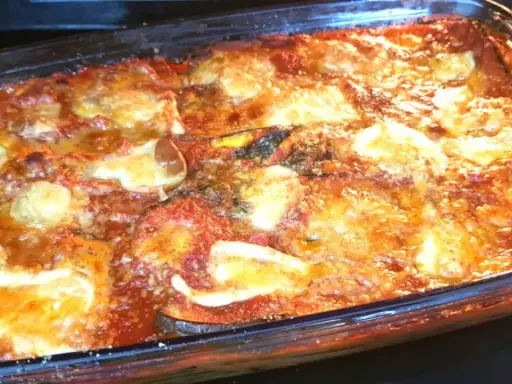 Parmigiana di melanzane appena sfornata, dorata e filante, in una teglia di vetro.