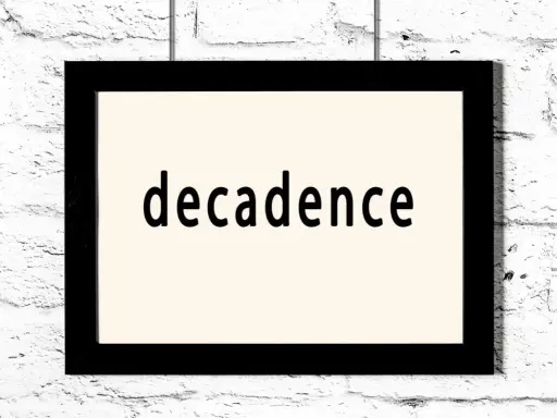 Czarny prostokątny obraz z napisem "decadence" na jasnym tle, wiszący na białej ceglanej ścianie. Symbol dekadentyzmu.