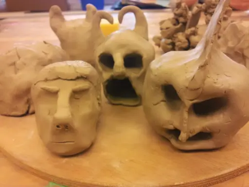 Flera ansikten och figurer i lera, skapade med fantasi. En del ser ut som monster, andra som människor.