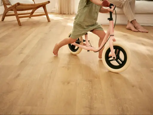 Un enfant apprend à faire du vélo d'équilibre sur un sol de salle de jeux en bois clair.