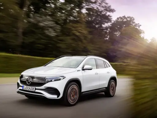 Un Mercedes EQA blanco circula por una carretera rodeada de árboles. Las **mercedes eqa medidas** son ideales para la ciudad y escapadas.