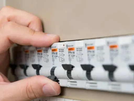 Main d'une personne actionnant un disjoncteur dans un tableau électrique. Les plombs ont sauté, il faut rétablir le courant.