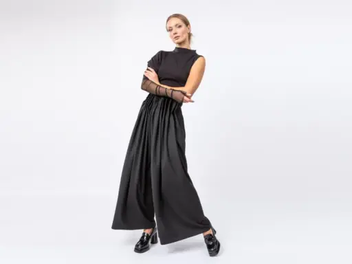 Elegancka kobieta w czarnych, szerokich spodniach i topie z siateczkowymi rękawami. Stylowe, lakierowane mokasyny to idealne buty do teatru.