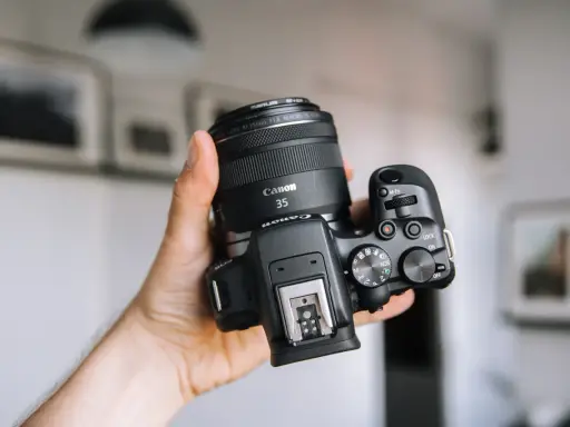 Dłoń trzyma aparat Canon z obiektywem 35mm, idealny dla amatora chcącego zacząć przygodę z fotografią.