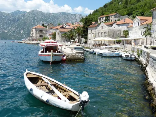 Port w Czarnogórze, łodzie na wodzie, góry w tle. Ceny rejsów mogą być różne, warto sprawdzić.