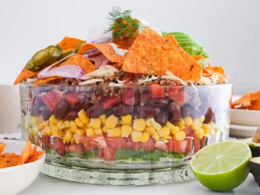 Schichtweise aufgebauter Taco Salat im Glas mit Hackfleisch, Bohnen, Mais, Tomaten, Salat, Nachos, Jalapeños und Avocado.