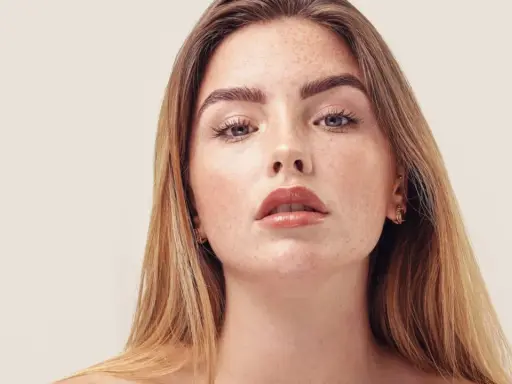 Nahaufnahme einer jungen Frau mit Sommersprossen und dunkelblond hellbraunen Haaren, die glänzend und glatt fallen.