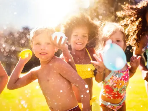 Niños riendo y jugando con globos de agua bajo el sol. Salpicaduras y diversión garantizada en estos juegos acuáticos.