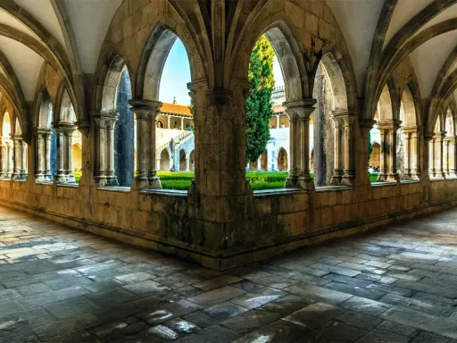 Gotische Arkaden im Kloster Batalha, Portugal. Sonnenschein fällt auf den Steinboden und beleuchtet den grünen Innenhof.
