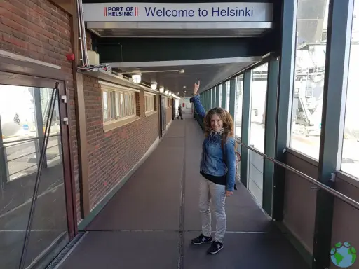 Mujer sonriente saluda bajo el cartel "Welcome to Helsinki". ¡Una aventura en Helsinki con niños comienza!