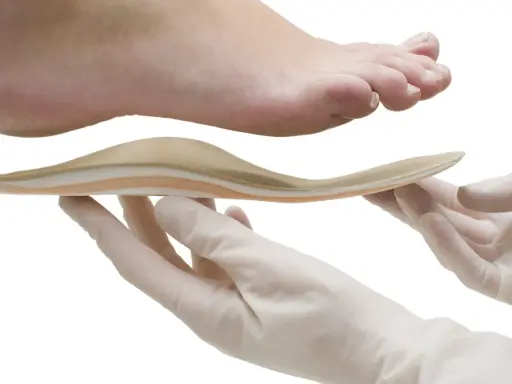 Une orthoplastie sur mesure est présentée sous un pied, tenue par des mains gantées.