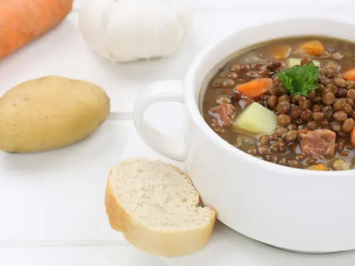 Herzhafte Linsensuppe nach DDR-Rezept mit Kartoffeln, Karotten und Speck. Dazu ein Stück Brot.