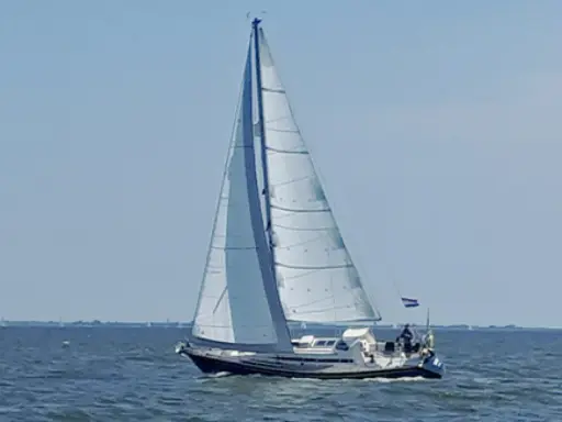Voilier blanc et bleu naviguant sur une mer calme sous un ciel clair. Les voiles sont gonflées par le vent. Les premiers 375 avis sur ce type de bateau sont positifs.