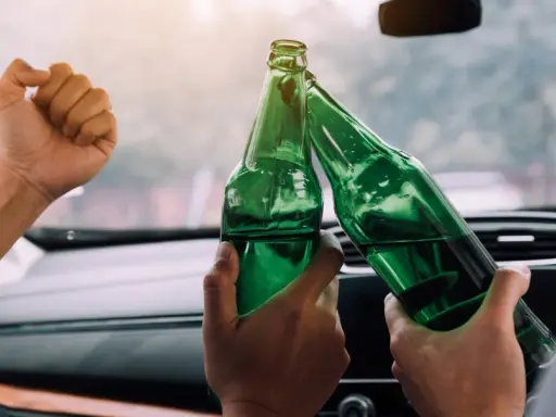 Dwie osoby w samochodzie wznoszą toast zielonymi butelkami piwa 0 5 procent.