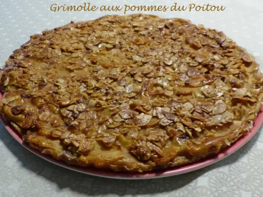 Gâteau rustique aux pommes et amandes effilées sur une assiette rose.