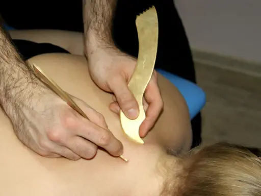 Terapeuta wykonuje zabieg pinopresury, używając złotych narzędzi do stymulacji punktów na plecach pacjenta.