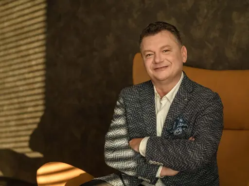 Uśmiechnięty mężczyzna, January Ciszewski, w eleganckiej marynarce siedzi w fotelu.
