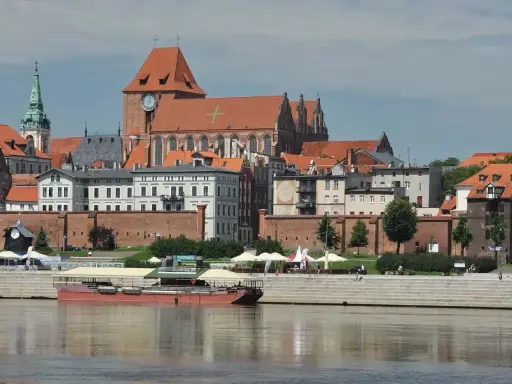 Widok na średniowieczny zespół miejski Torunia z Wisły. W oddali katedra i kamienice, na pierwszym planie barka.