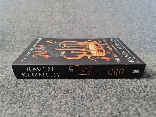 Okładka książki "A Gilded Cage is Still a Prison" autorstwa Raven Kennedy. Złota klatka i płomienie na ciemnym tle.