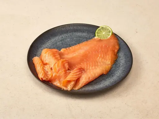 Räucherlachs auf dunkler Platte, garniert mit einer Limettenscheibe. Perfekt für einen Caipirinha-Lachs-Genuss.