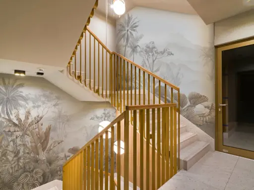 Habillage mur cage d'escalier avec un décor tropical en camaïeu. Escalier en marbre et rambarde en bois doré.