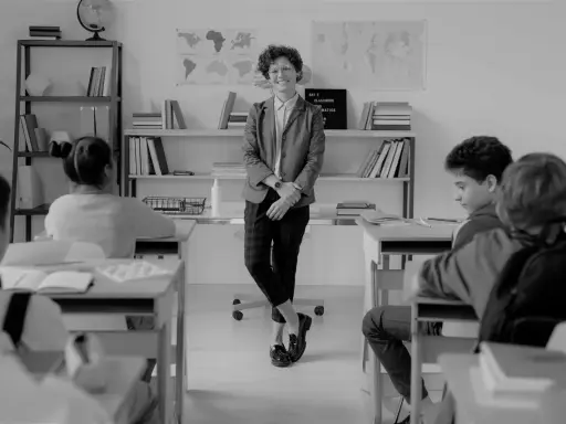 Lehrerin lächelt in einem Klassenzimmer, während Schüler an ihren Tischen sitzen. Eine Szene, die eine gute Klassengemeinschaft widerspiegelt.