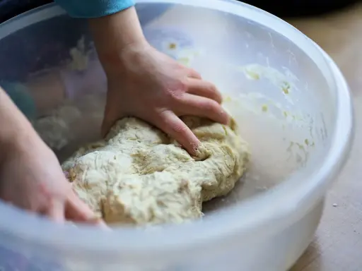 Mains d'enfant pétrissant une pâte à pizza dans un bol. Une étape clé de la recette pâte à pizza levure sèche.