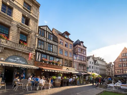 Terrasses animées devant les maisons à colombages de l'incontournable Rouen, sous un ciel bleu éclatant.