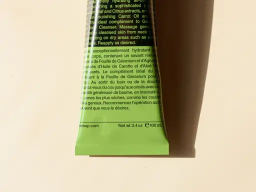Tubo verde brillante di Aesop con testo in inglese e francese. Il testo descrive un balsamo corpo idratante, spiegando il suo inci significato e gli ingredienti chiave.