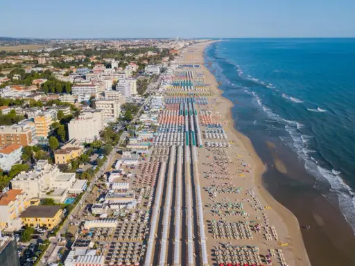 Vista aerea delle frazioni di Rimini: una lunga spiaggia attrezzata con file ordinate di ombrelloni e lettini, hotel e palazzi affacciati sul mare Adriatico.