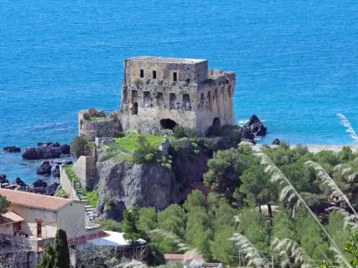 Torre aragonese a picco sul mare, uno dei borghi da visitare in Calabria, con case e vegetazione lussureggiante.
