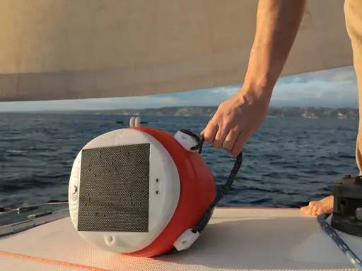 Main tenant une bouée orange et blanche, prêt à la mouiller à hauteur. La mer et le ciel bleu en arrière-plan.