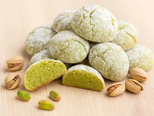 Amaretti pistache saupoudrés de sucre glace, avec des pistaches entières et décortiquées. Une recette gourmande à découvrir.
