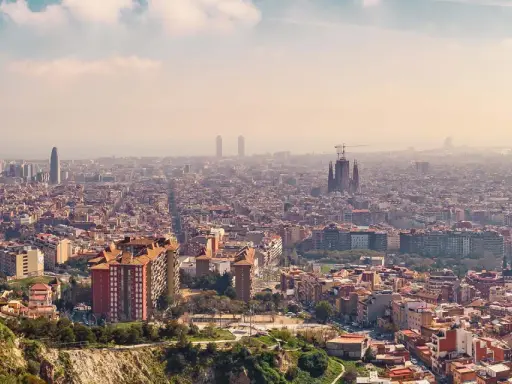 Panorama von Barcelona von oben. Die Sagrada Familia und moderne Wolkenkratzer ragen aus der weitläufigen Stadt hervor.