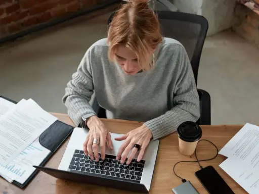 Kobieta pracuje przy laptopie, analizując dokumenty. Zastanawia się, czy umowa zlecenie wlicza się do stażu pracy, szukając odpowiedzi online.