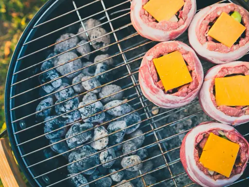 Fem baconsnurrade köttfärsbiffar med ost på en grill för indirekt grillning.