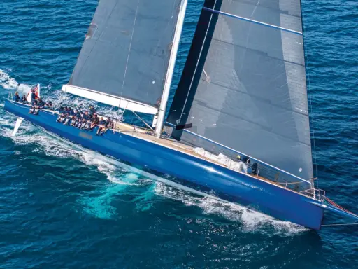 Un grand voilier bleu glisse sur l'eau, tel un tapis volant bateau. L'équipage est à bord, profitant de la navigation.