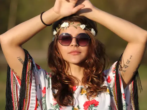 Dziewczyna w stylu boho, z wiankiem z kwiatów i okularami, w kwiecistej bluzce. Jej moda nawiązuje do wolności i natury, jak u dzieci kwiatów.