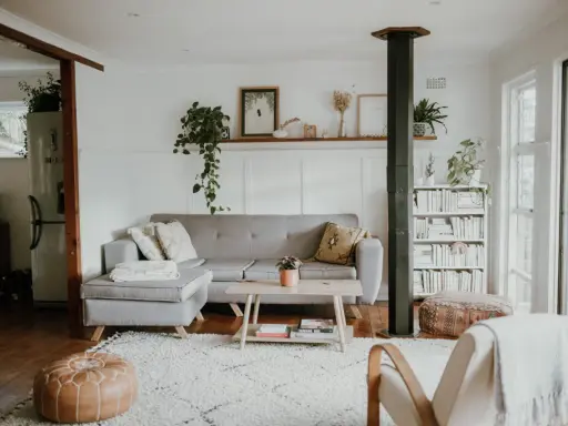 Przytulny salon w stylu skandynawskim nowoczesnym. Szara kanapa, drewniany stolik, regał z książkami i mnóstwo zieleni tworzą relaksującą atmosferę.