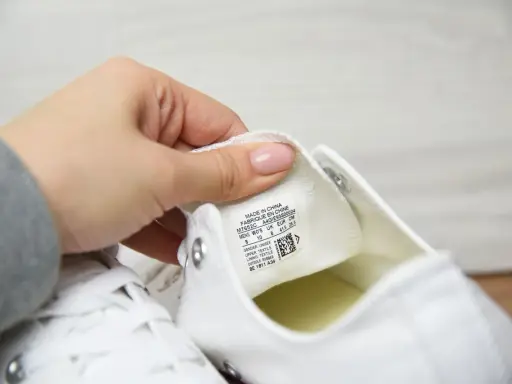 Dłoń pokazuje metkę z rozmiarem na białych butach Converse. Sprawdzamy, czy to oryginalne Converse, a nie podróbki.