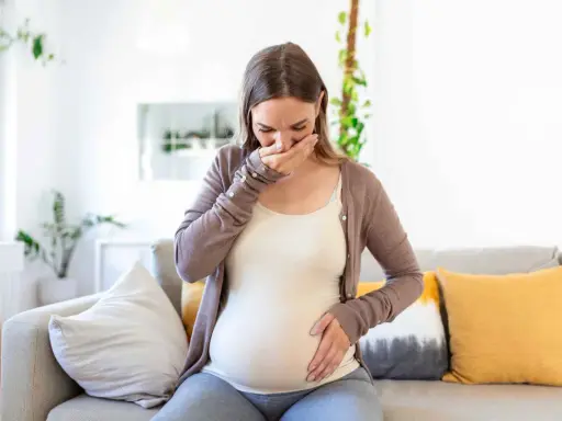 Donna incinta con nausea nel terzo trimestre, copre la bocca con la mano.