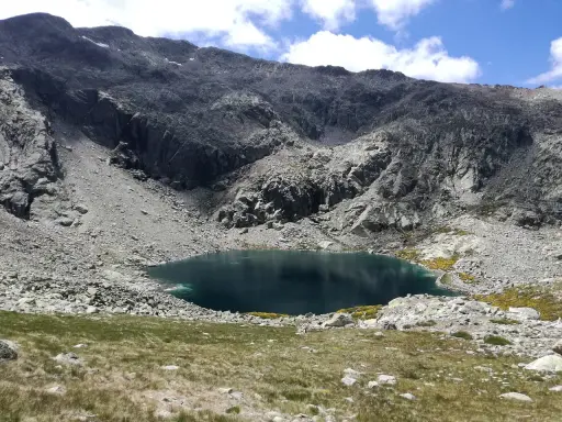 Ein tiefblauer Bergsee in der Sierra de Gredos, umgeben von felsigen Hängen und grünen Wiesen.