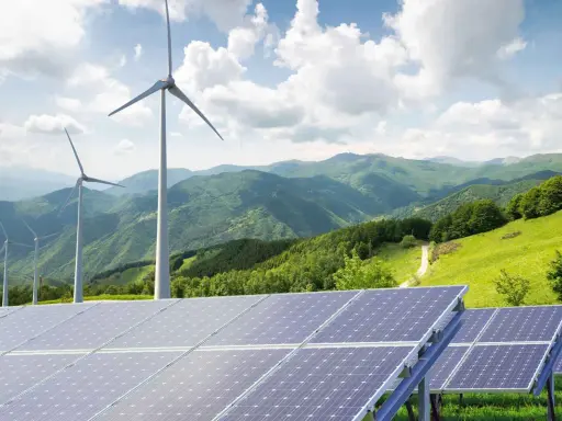Paneles solares y aerogeneradores en un paisaje montañoso verde. La energía renovable, como la solar y la eólica, complementa la idea de un futuro sostenible, similar a cómo un generador de biomasa podría integrarse.