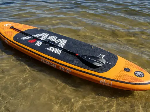 Pomarańczowy aquamarina sup z wiosłem leży na płytkiej, przejrzystej wodzie.